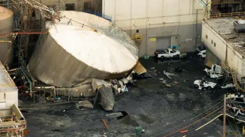 The ruptured tank, with crushed cars in the foreground