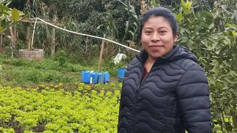 BBC Farmer Sandra Noemi Buku Saaz stands in front of her land and smiles at the camera