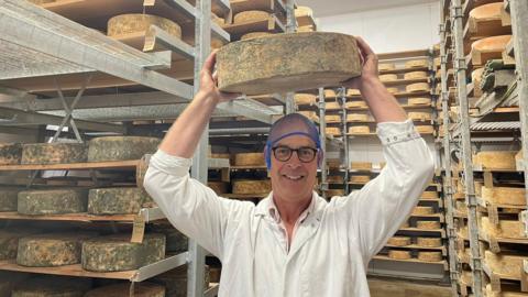 David Clarke in his cheese 'cave' holding up one of his Red Leicester cheeses 