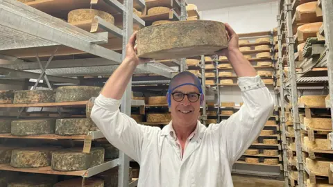 BBC David Clarke in his cheese 'cave' holding up one of his Red Leicester cheeses 