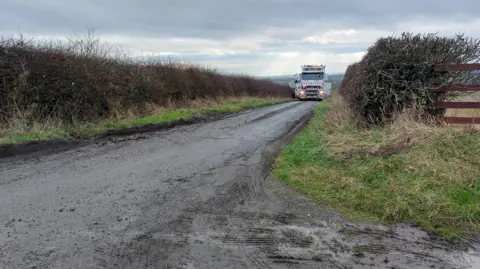 Deborah Wong A lorry makes its way slowly along a narrow country lane.