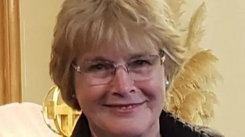 CHRISTINE PAIN Christine, a woman with short blonde hair, with reading glasses, she smiles.