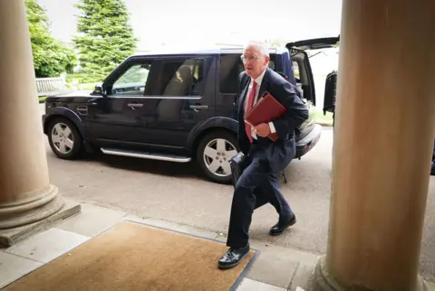 Press Eye/PA Hilary Benn walks past jeep and done pillars astatine entranceway to Hillsborough Castle