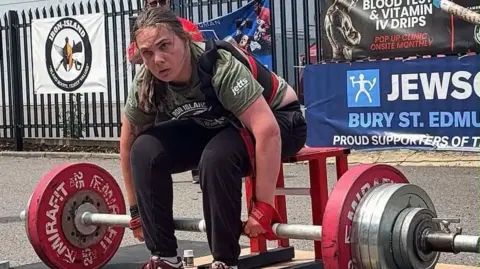 A woman sitting on a bench holding a barbell with large Mirafit weights on either side.