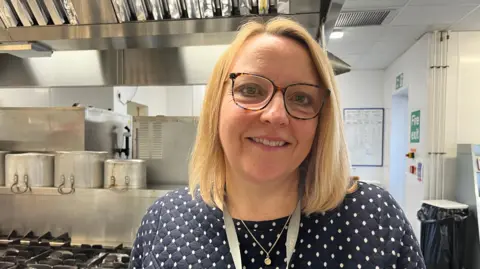 A woman with blonde hair and glasses standing in a school kitchen