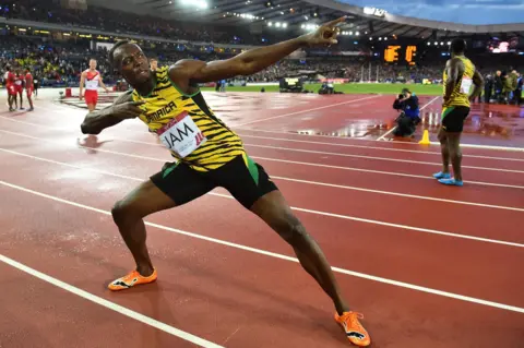 Getty Images Usain Bolt is wearing colourful yellow, black and green running kit while striking a pose on a running track. 