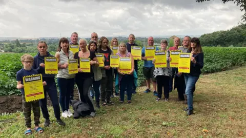 LDRS Members of the campaign group I Love Heath Common holding yellow placards and standing in front of a field