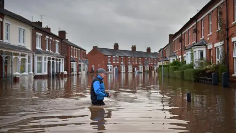 Getty Images A Carlisle resident makes his way through floodwater. Red brick terraced houses on both sides of the road are submerged.