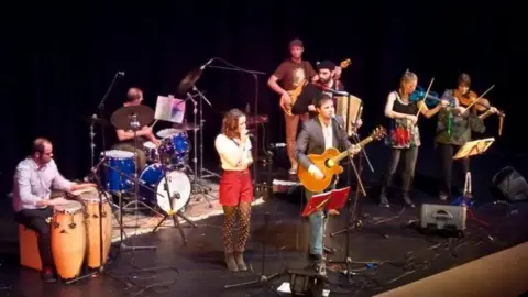 A band including drummers, guitarists and singers perform on stage.