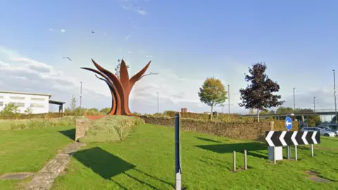 A metallic sculpture in the middle of a grassy roundabout