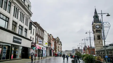 Darlington high street. A House of Fraser store is among a number of shops on the left side of the street. A clock tower stands on the right.