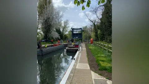 Work being carried out on a lock. A team of people are dotted around the canal on a clear day.