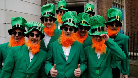 REUTERS/Clodagh Kilcoyne A group of nine young men dressed as leprechauns, with matching green suits and fake orange beards.  The man in the middle is posing with his thumbs up. 