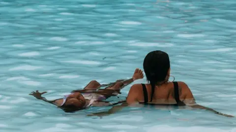 EPA/Shutterstock A woman and child soak in a pool 