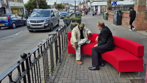 Hector Pinkney AKA 'Mr Handsworth' sits on the red sofa on Soho Road in Birmingham