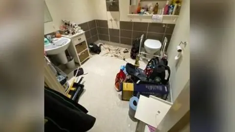 LDRS A bathroom with a number of items on the floor, including blue roll, a dust sheet, a backpack and some tools.