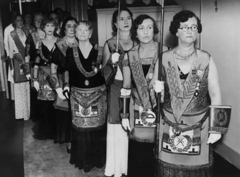 Gamma-Keystone via Getty Images A group of women in ceremonial robes stand in line in a room during the consecration of the first women's masonic temple takes place at St Ermins, Westminster in 1933.