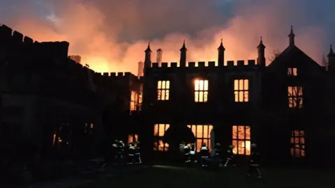 Craig Baker/Dorset and Wiltshire Fire Service Parnham House is silhouetted by a fire which glows through ground and first floor windows and lights up clouds of smoke above the roof.