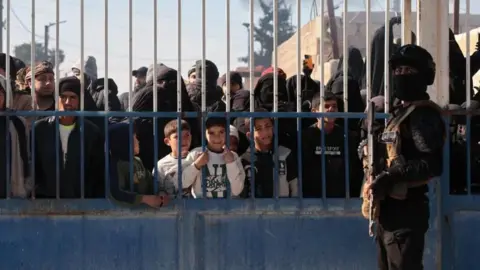 man stands in front of gate with prisoners behind