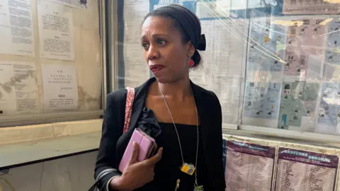 Aysha Bell stands in a building in Hong Kong holding a bag. 