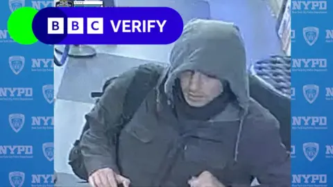 The "wanted individual" wearing a grey hoodie and jacket, with a mask wrapped around his neck and wearing a black backpack