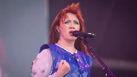 CMAT, dressed in a bright and shiny blue top, sings during day three of Glastonbury festival 2025 at Worthy Farm in Pilton, Somerset. 