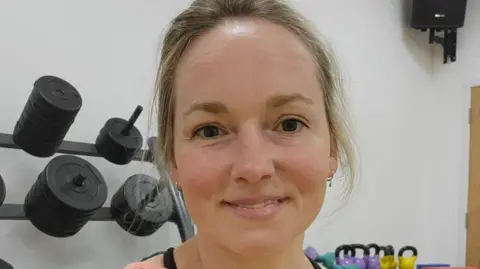Suzanne Brazier Emma, a woman with tied back light brown hair, smiling for camera.