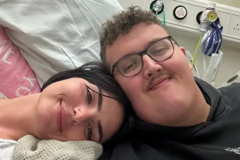 Marshall Exler A smiling couple lay together on a hospital bed in a selfie