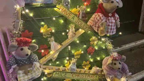 Three felt mice, wearing knitted clothes, against a green background. There is also a sign that reads heave a jolly mice Christmas