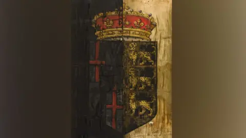 The Cromwell Museum A 17th Century funeral banner from Oliver Cromwell's state funeral. It shows a shield with three leopards on the right and two red crosses on the left. Above the shield is a crown in gold and red