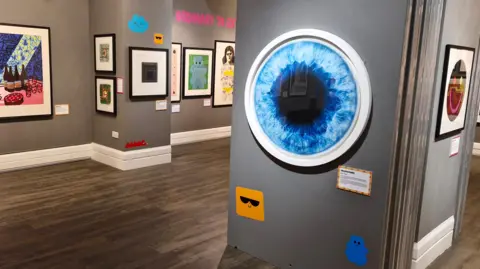 SUZANNE WALKER The display, you can see one, which is a blue circle with darker blue inside resembling an eye, another shows food and drink on a table.