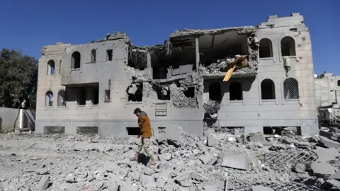 AFP A Yemeni man checks the remains of a Houthi-run detention centre in the capital Sanaa after a Saudi-led coalition air strike (13 December 2017)