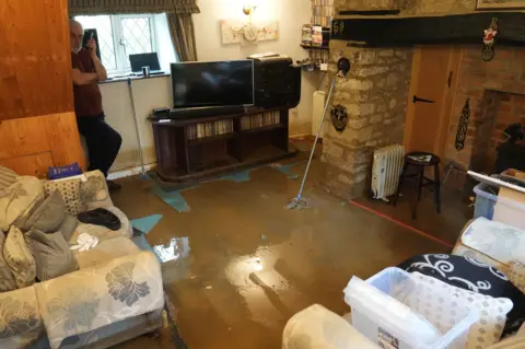 PA Media Tim Mayer stands in his living room which in his Northamptonshire home which has been damaged by flood water