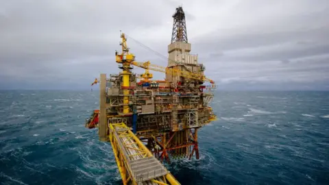 Getty Images An oil rig in choppy blue waters in the North Sea. The structure is made up of yellow, red and blue pipes and beams, with a tower on the right hand side extending into a grey sky