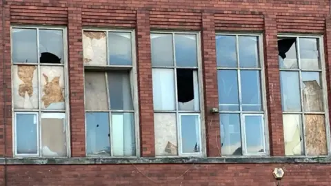 Five broken windows on a red brick building