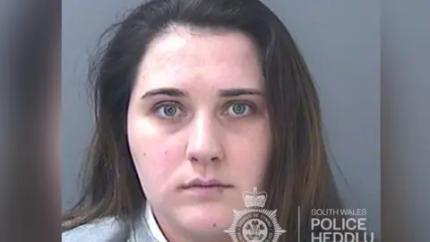 South Wales Police Custody image of Jodie Beer who has freen eyes and long dark hair and is wearing a grey sweatshirt