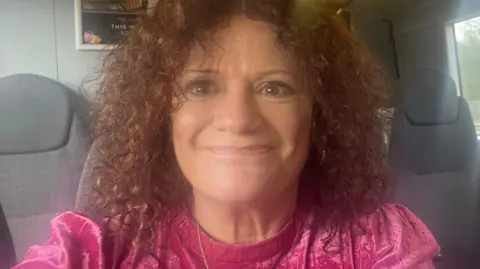 Charlotte Bingley A woman looks straight at the camera. She has curly brown hair and is wearing a pink top