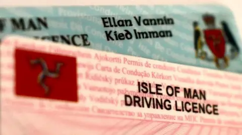 Two Isle of Man driving licences on top of each other - one on top is pink, the other is blue.