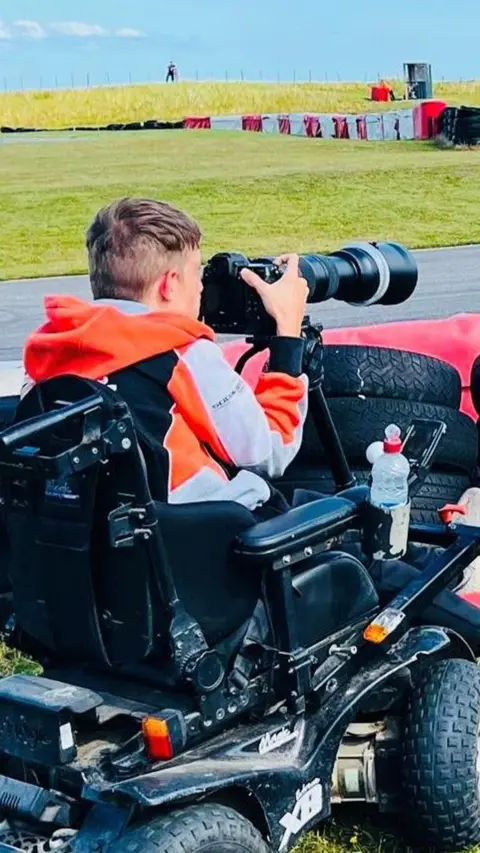 Jake Smith - man in an electric wheelchair, holding a large lens camera at a racetrack