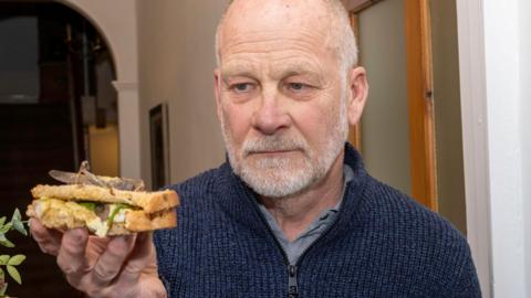 Phil Hall holds sandwich with locust on it