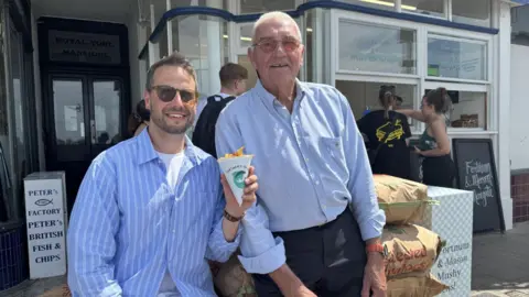 Antonio Zoccola with the Fortnum's branded cone of chips with shop owner Peter Curtis outside Peter's Fish Factory in Margate.