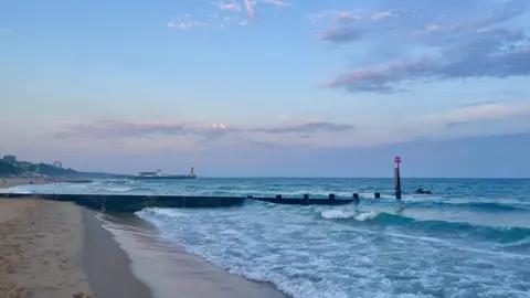 Amanda Norfolk The sandy beach on the left and the blue and white ocean on the right with waves crashing on the shore.
