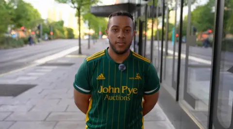 Jack Hudson, 21, electrician from Nottingham, stands in a busy street with his arms behind his back, wearing a cricket T-shirt