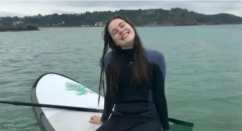 Megan McDonagh Lily sat on a paddle board in a wetsuit smiling at the camera 