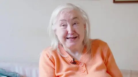 Cornelia McCarthy sat on her sofa in an orange knitted t-shirt.
