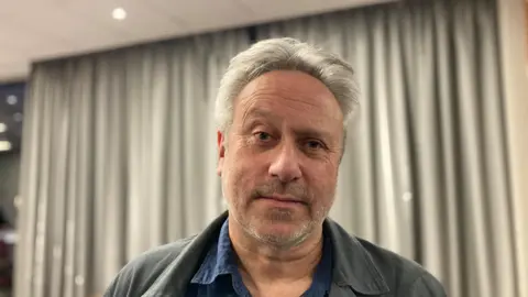 BBC/Laura Coffey Man looking at the camera wearing a blue jacket and blue shirt