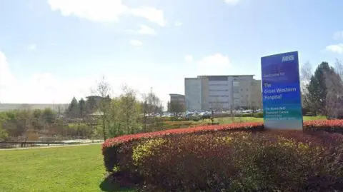 Google Maps Hospital entrance under sunny sky showing green lawns, pond and large entrance sign.