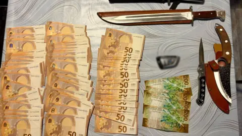 Bank notes are lined up on a table. They are mainly 50 Euro notes. There are also several knives.