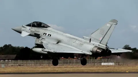 A grey Typhoon jet takes off on a runway with streams coming out of its exhaust.