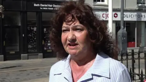 BBC Caroline Jones is wearing a blue shirt while standing in a street